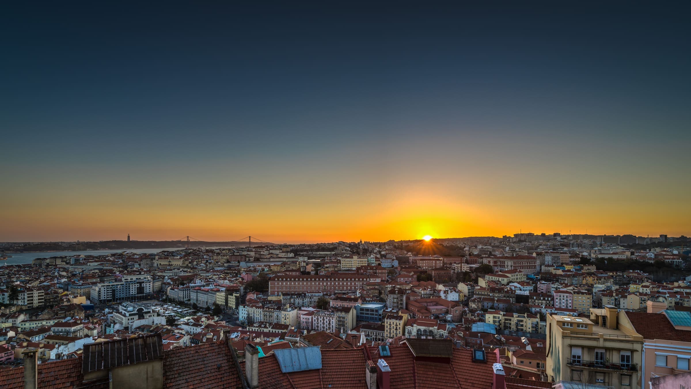 Vista de Lisboa ao anoitecer, telhados da cidade sob um céu dourado